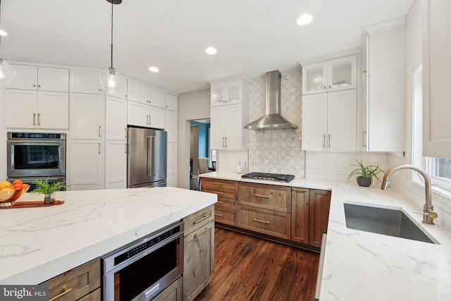 kitchen with tasteful backsplash, stainless steel appliances, wall chimney range hood, white cabinetry, and a sink