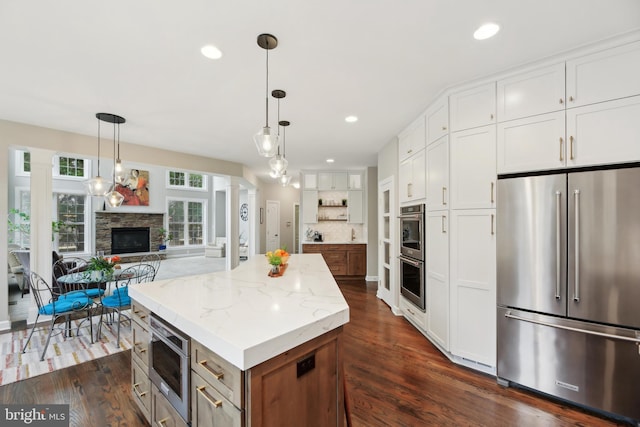 kitchen with white cabinets, dark wood finished floors, a kitchen island, stainless steel appliances, and a stone fireplace