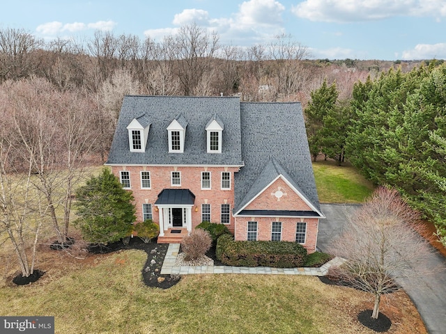 colonial house with brick siding, a front lawn, and a shingled roof