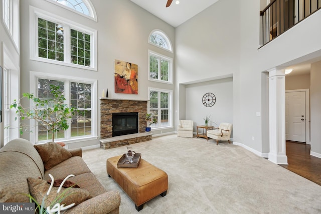 living area with baseboards, a ceiling fan, carpet floors, ornate columns, and a fireplace