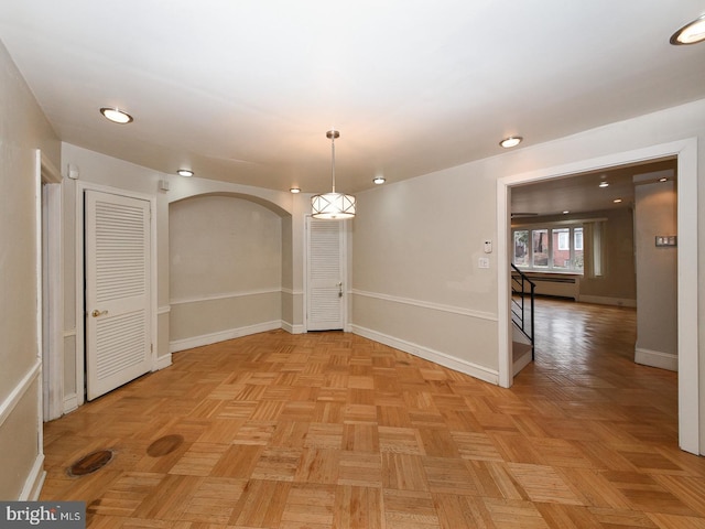 empty room featuring arched walkways, a baseboard radiator, and baseboards