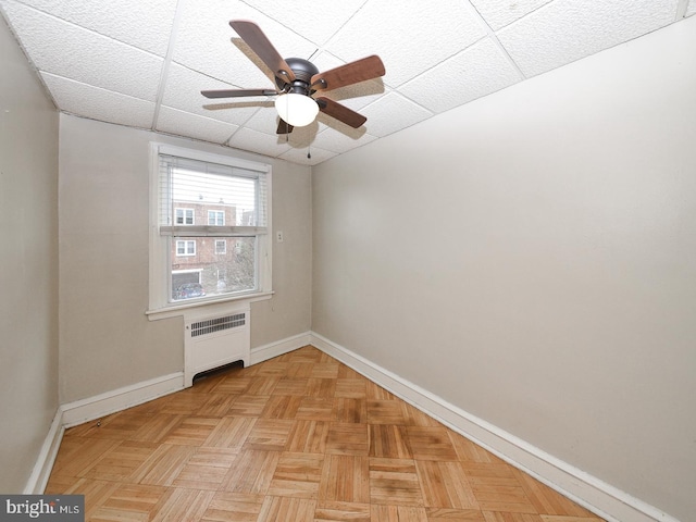 empty room featuring radiator, a ceiling fan, baseboards, and a drop ceiling