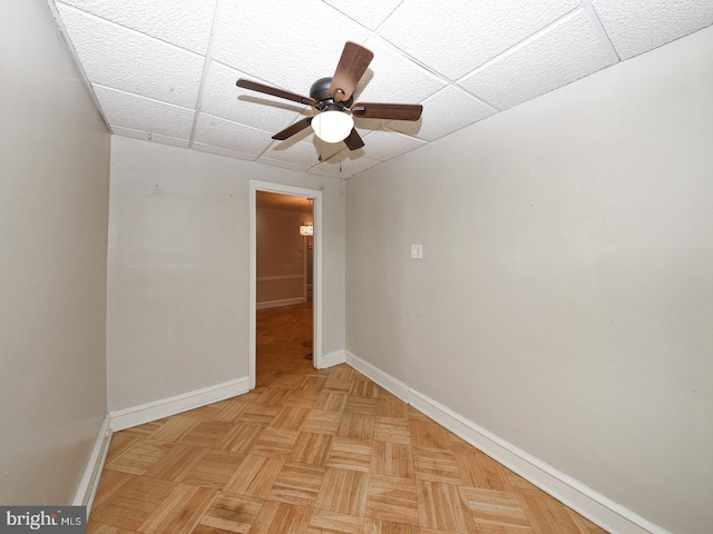 unfurnished room with a paneled ceiling, ceiling fan, and baseboards