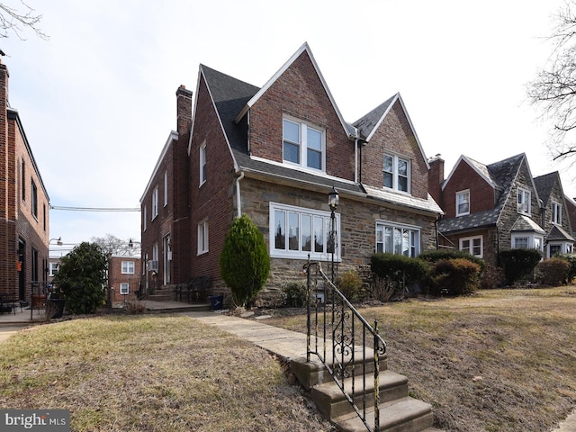 view of front of property with a front yard, stone siding, a chimney, and entry steps