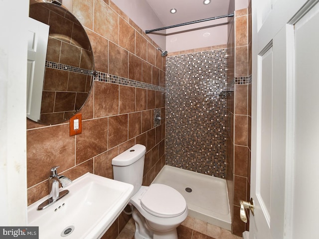 full bathroom with tiled shower, a sink, toilet, and tile walls