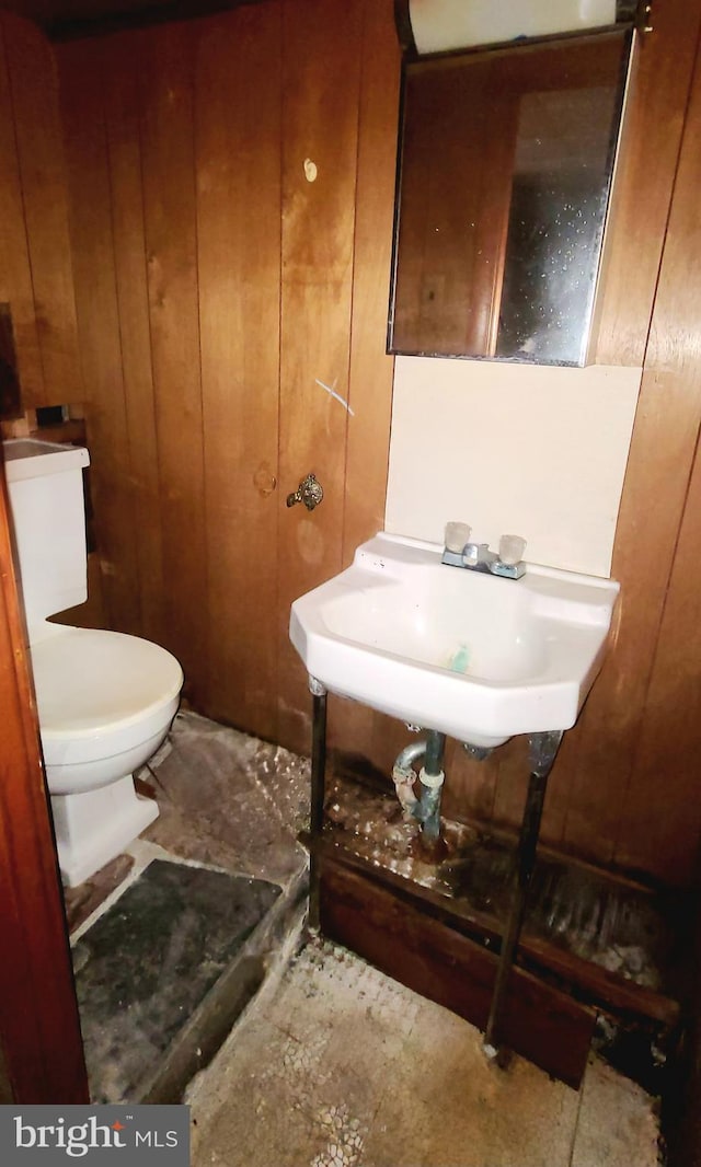 half bathroom featuring toilet, wooden walls, and a sink