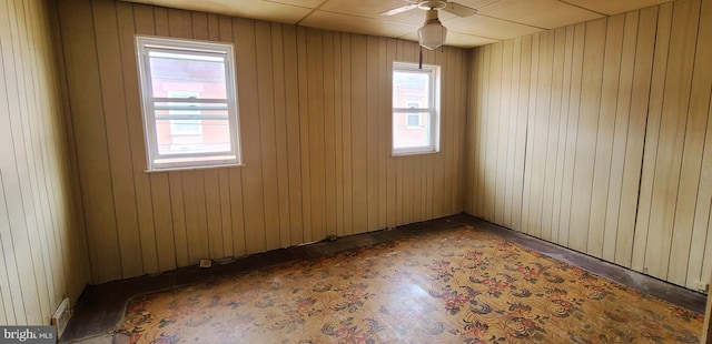 unfurnished room featuring plenty of natural light, wooden walls, and ceiling fan