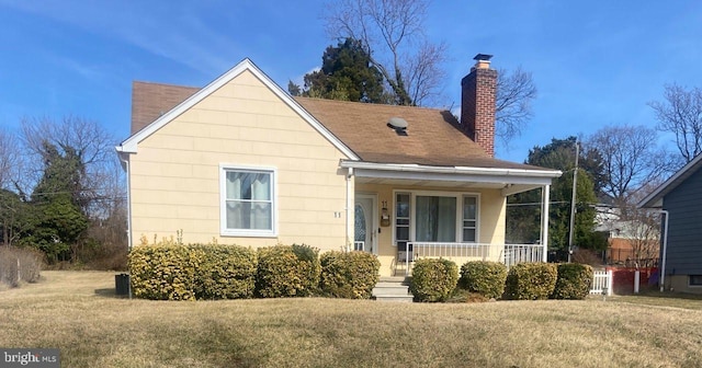 bungalow featuring covered porch, a chimney, a front yard, and a shingled roof