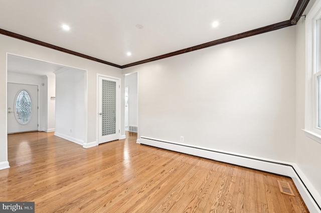 empty room with light wood finished floors, baseboards, crown molding, and a baseboard heating unit