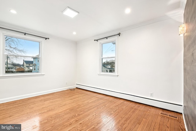 empty room with a baseboard heating unit, crown molding, baseboards, and wood finished floors