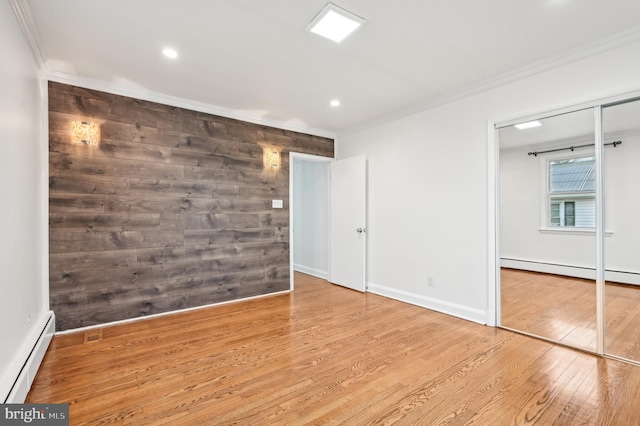 empty room featuring a baseboard radiator, baseboards, crown molding, and hardwood / wood-style floors