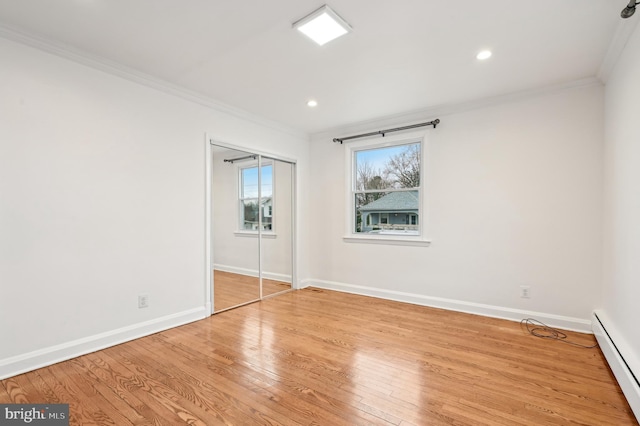 unfurnished bedroom with baseboards, a baseboard heating unit, crown molding, and wood finished floors