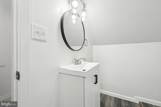 bathroom with vaulted ceiling, vanity, baseboards, and wood finished floors