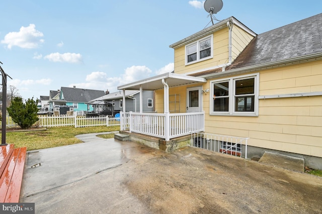 exterior space with a porch, fence, roof with shingles, a lawn, and a residential view