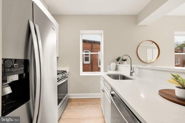 kitchen with a sink, white cabinets, light countertops, appliances with stainless steel finishes, and light wood-type flooring