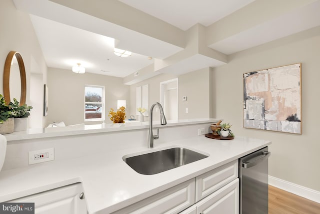 kitchen featuring light countertops, light wood-style flooring, stainless steel dishwasher, white cabinetry, and a sink