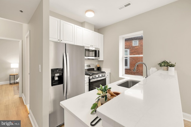 kitchen with stainless steel appliances, visible vents, light wood-style flooring, white cabinetry, and a sink