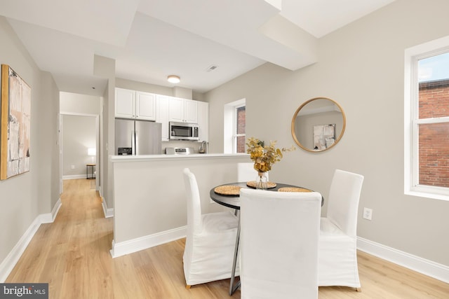 dining space with a wealth of natural light, light wood-style flooring, and baseboards