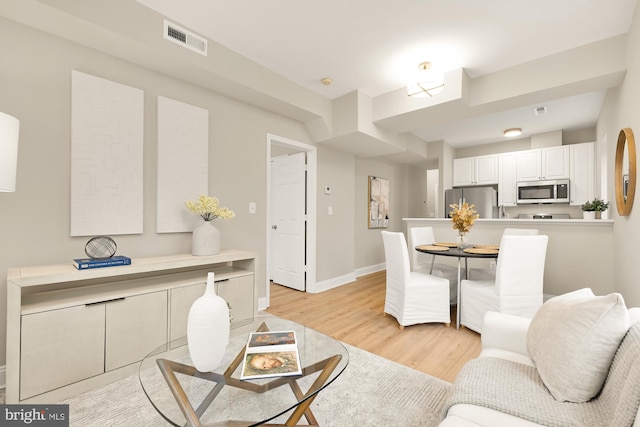 living room featuring light wood-type flooring, visible vents, and baseboards