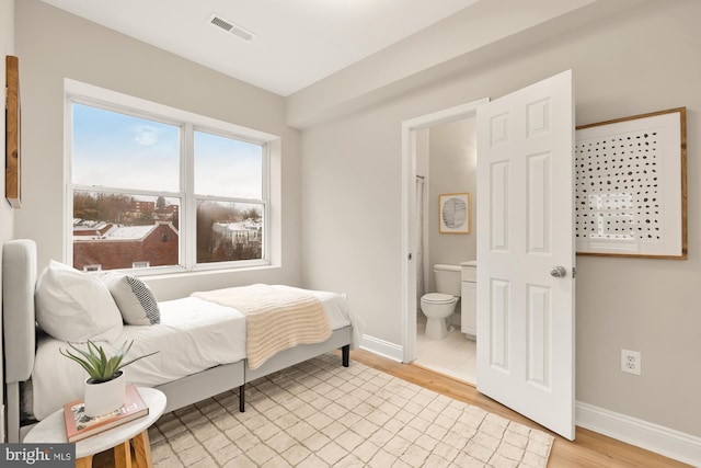 bedroom with light wood-type flooring, visible vents, connected bathroom, and baseboards