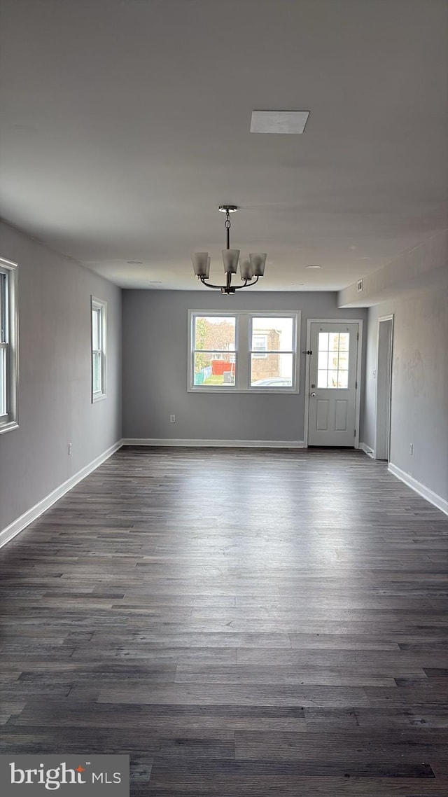 unfurnished dining area featuring dark wood-style floors, baseboards, and a chandelier