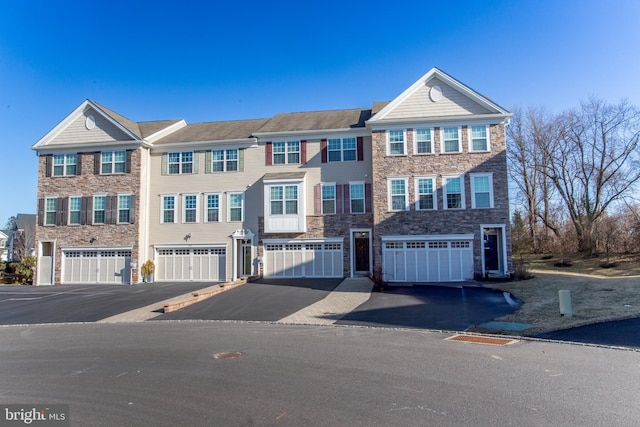 townhome / multi-family property featuring driveway, stone siding, and an attached garage