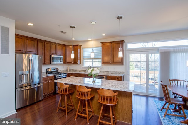 kitchen with stainless steel appliances, brown cabinets, dark wood finished floors, and light stone counters