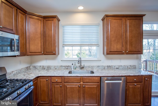 kitchen with stainless steel appliances, brown cabinetry, a sink, and light stone counters