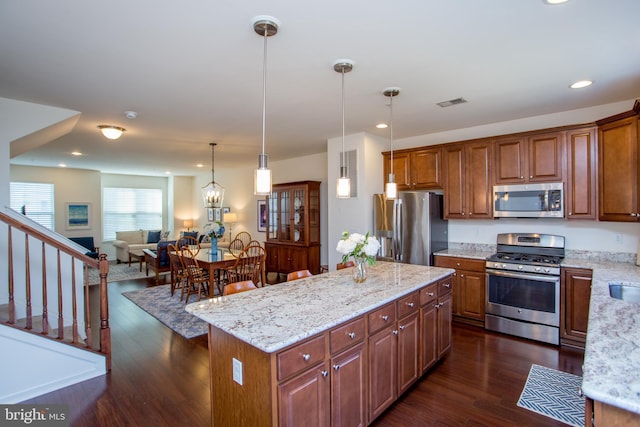 kitchen featuring a kitchen island, appliances with stainless steel finishes, dark wood finished floors, and light stone counters