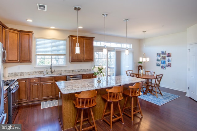 kitchen featuring a breakfast bar area, stainless steel appliances, a sink, brown cabinets, and dark wood-style floors