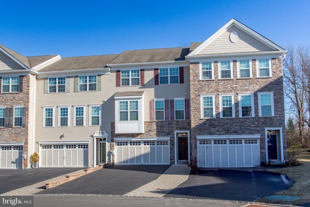 multi unit property featuring driveway, stone siding, and an attached garage