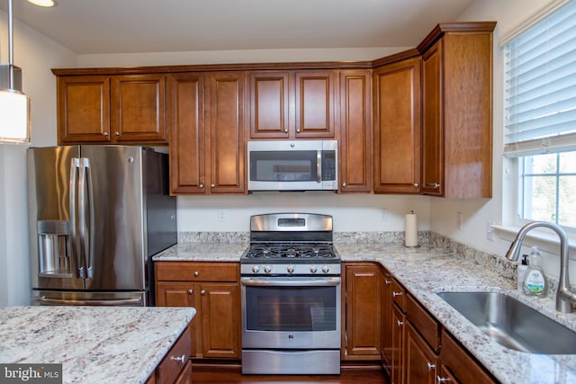 kitchen featuring appliances with stainless steel finishes, brown cabinetry, a sink, and light stone counters