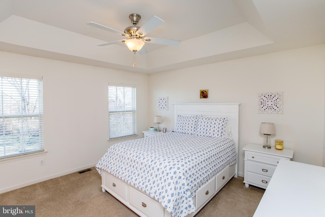 bedroom featuring light colored carpet, a ceiling fan, baseboards, visible vents, and a tray ceiling