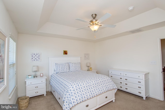 bedroom with ceiling fan, light carpet, visible vents, baseboards, and a tray ceiling