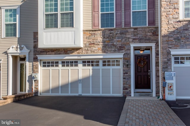 view of exterior entry with stone siding, aphalt driveway, and an attached garage