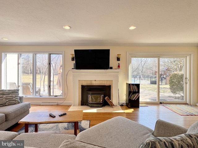 living area with a textured ceiling, recessed lighting, wood finished floors, a wood stove, and crown molding