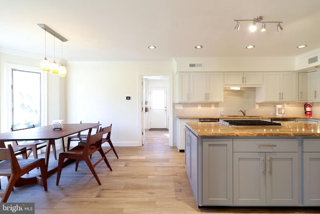 kitchen with crown molding, tasteful backsplash, visible vents, light stone countertops, and light wood-type flooring