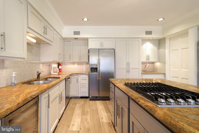 kitchen featuring light stone counters, beverage cooler, a sink, appliances with stainless steel finishes, and ornamental molding