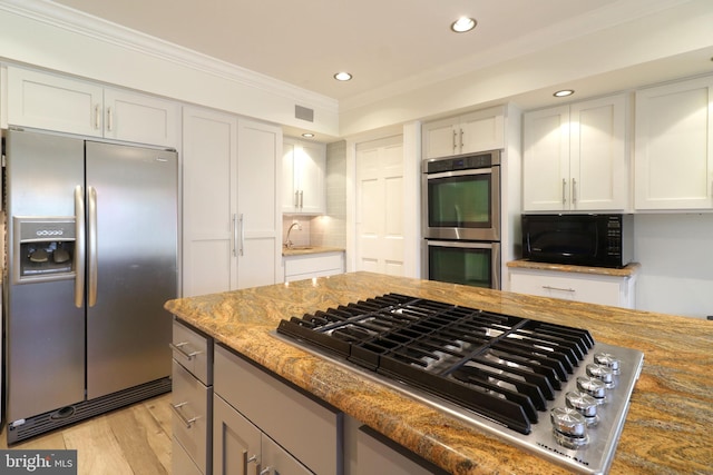 kitchen featuring light wood finished floors, tasteful backsplash, white cabinets, appliances with stainless steel finishes, and crown molding