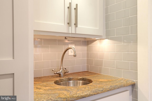 kitchen featuring light stone countertops, white cabinetry, decorative backsplash, and a sink