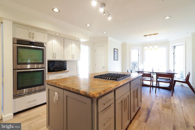 kitchen with a center island, light stone countertops, stainless steel appliances, crown molding, and light wood-style floors