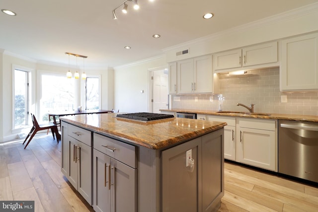 kitchen with ornamental molding, stainless steel appliances, light wood finished floors, and a sink