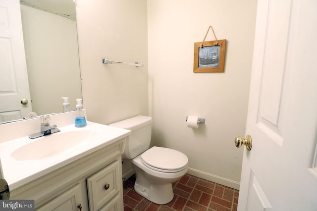 half bath with toilet, brick floor, baseboards, and vanity