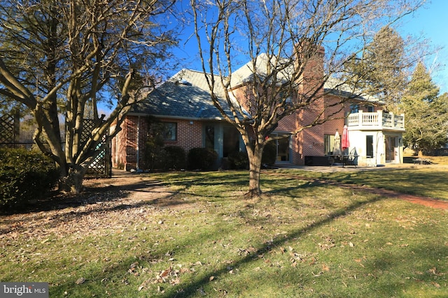 exterior space featuring a patio, brick siding, a front lawn, and a balcony