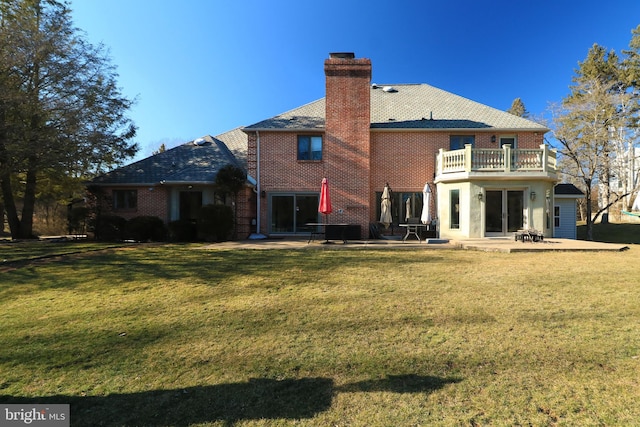 back of house featuring brick siding, a chimney, a lawn, a patio area, and a balcony