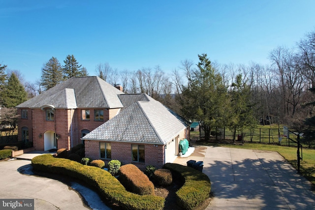 view of side of property featuring a chimney, fence, concrete driveway, and brick siding