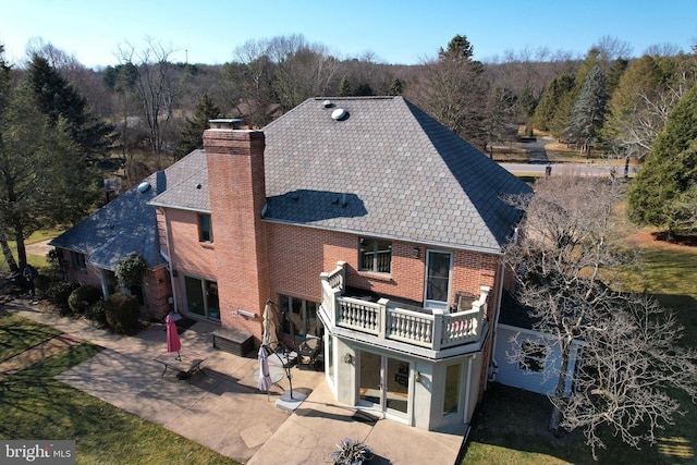 rear view of property with a patio, a balcony, a forest view, a chimney, and brick siding