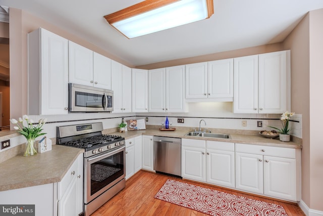 kitchen with appliances with stainless steel finishes, light countertops, light wood-style floors, white cabinetry, and a sink