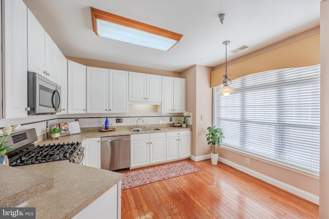 kitchen with pendant lighting, visible vents, light wood-style flooring, appliances with stainless steel finishes, and a sink