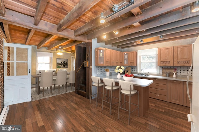 kitchen with dark wood-style floors, a peninsula, decorative backsplash, light countertops, and a kitchen bar